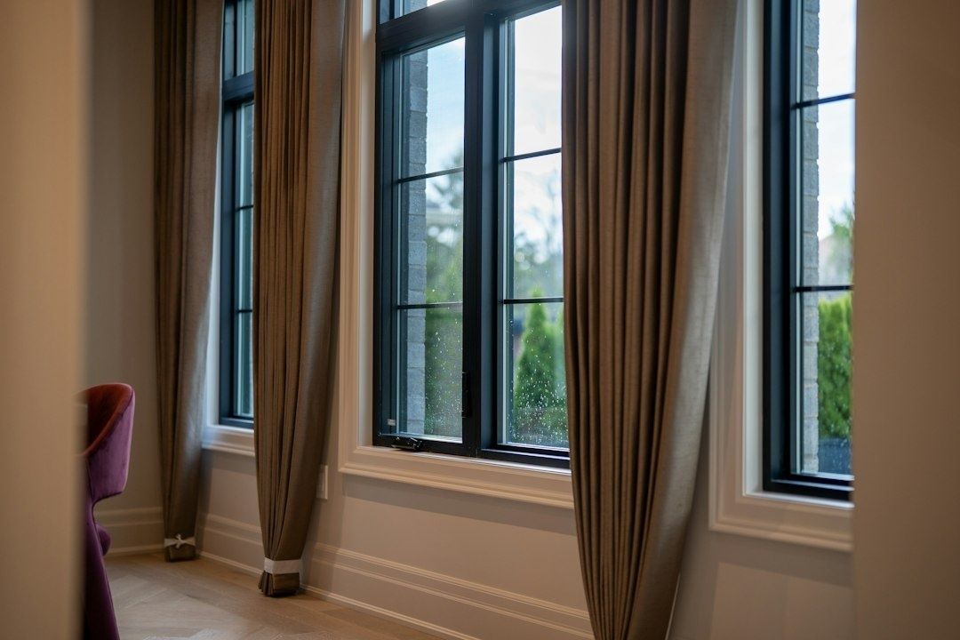 Schwere Vorhänge rahmen mehrere große Fensterfronten in einem hellen Raum